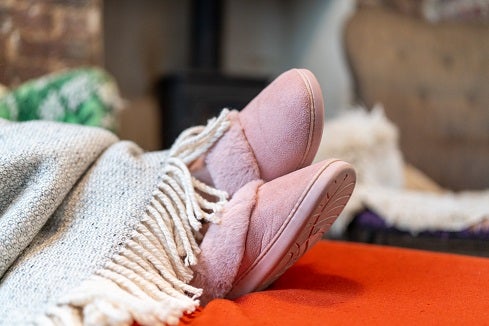 Cropped shot of a homeowners legs wearing pink slippers rested on a foot stool covered by a grey blanket