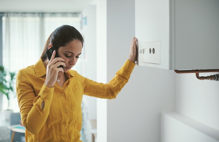 Young brunette Caucasian woman on the phone with her hand rested against a boiler