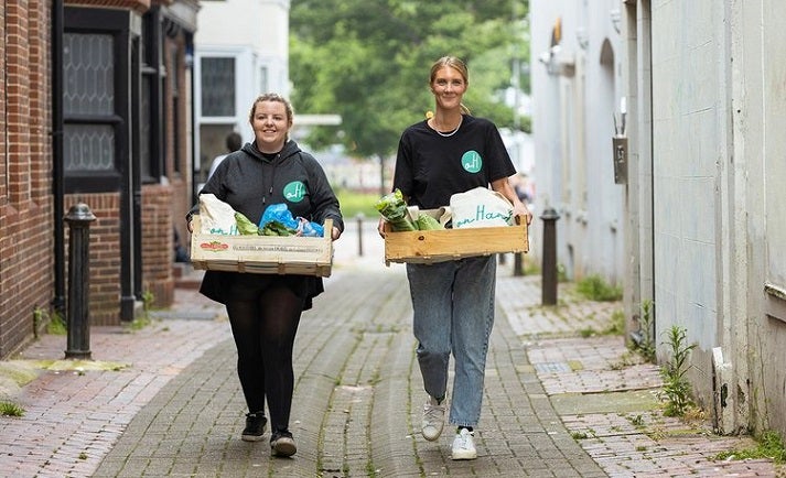 Two females volunteering for onHand walking through a street carrying hampers full of fresh food