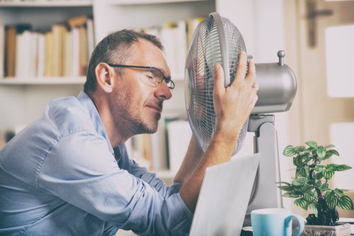 Middle aged Caucasian man sitting at an office desk in front of a fan to cool down