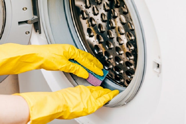 Cropped shot of male hands wearing yellow rubber clothes cleaning the door seals on a washing machine with a sponge