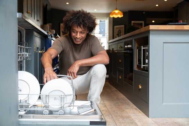 Young mixed race dad loading white plates in to the dishwasher