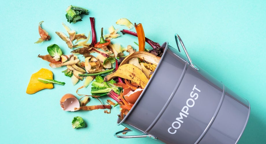 Food falling out of a grey compost bin on a blue background