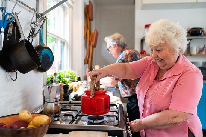 Elderly woman using gas cooker to boil a kettle
