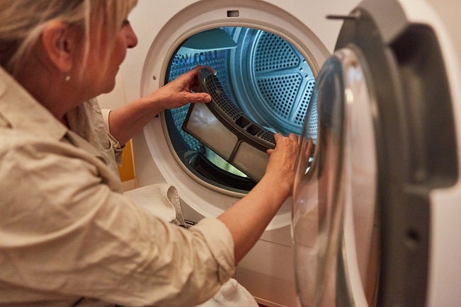 Middle-aged blonde Caucasian woman cleaning the lint filter of a tumble dryer