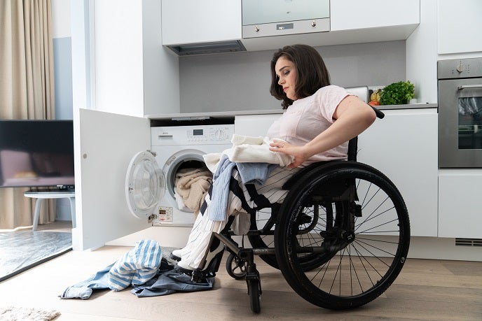 Mother in a wheelchair loading clothes into the washing machine
