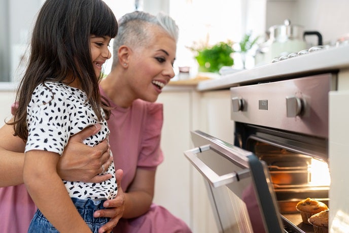 Mother and daughter smiling whilst looking at muffins baking in the oven